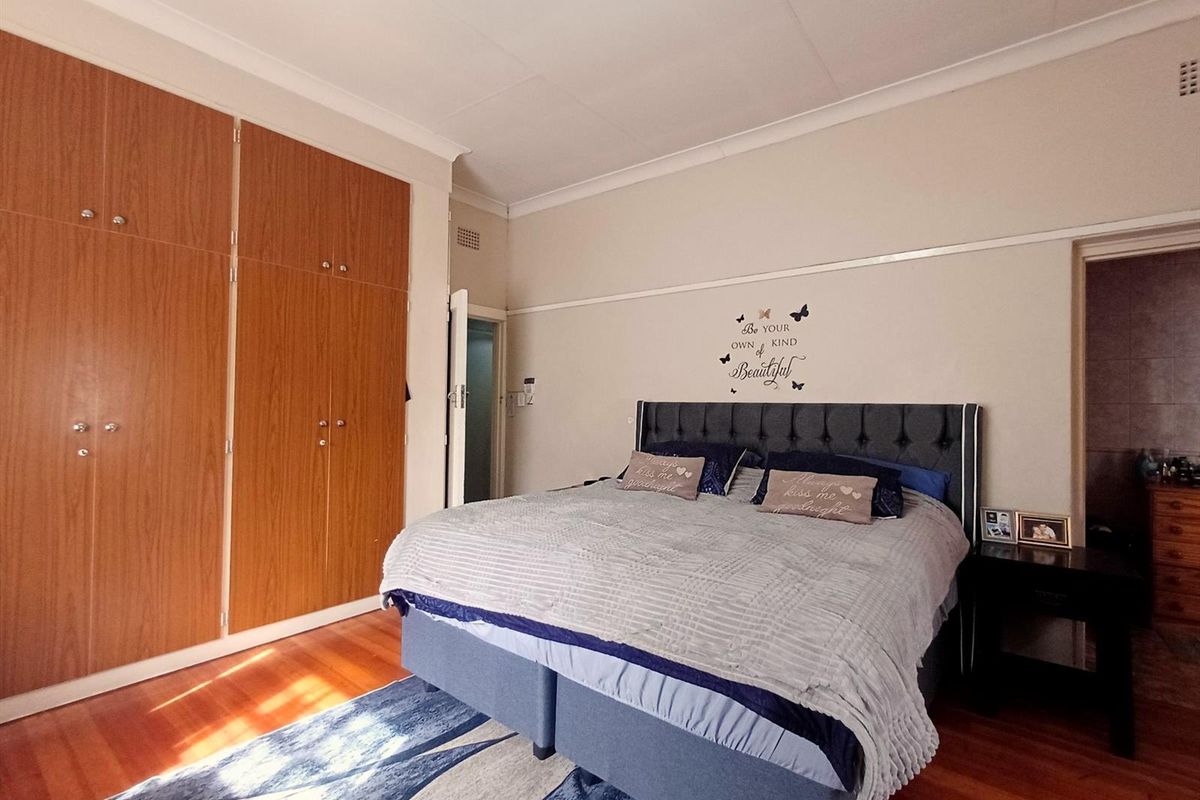 A well-maintained bedroom featuring polished hardwood flooring, classic picture rails, and extensive built-in wooden wardrobe storage.