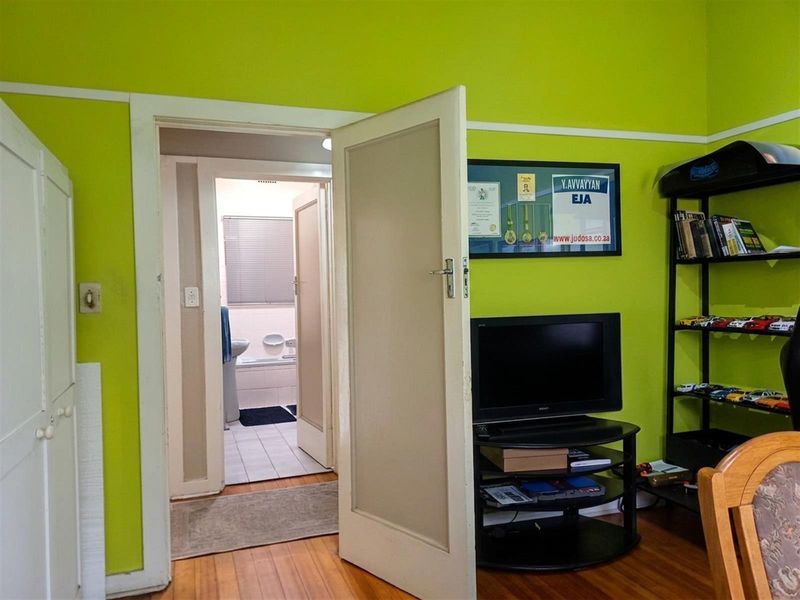 A bedroom featuring hardwood flooring and a view into an adjacent bathroom, with bright green wall paint and traditional timber door frames.