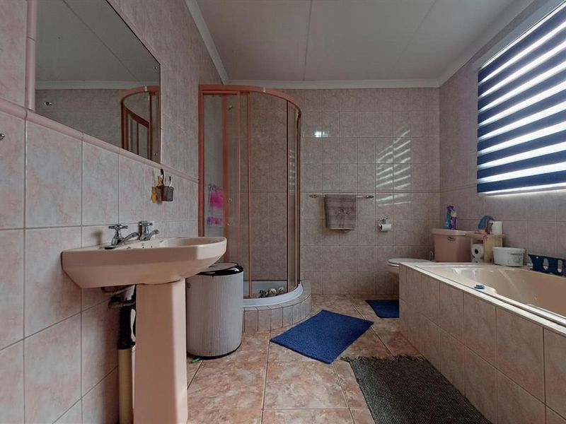 A functional bathroom featuring a pedestal basin, corner shower, built-in bathtub, and toilet, finished with neutral wall and floor tiling.