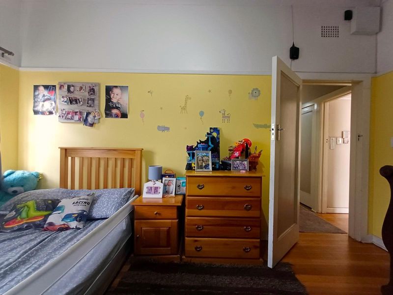 A bedroom featuring timber flooring and a classic picture rail, currently utilized as a child's room with yellow painted walls.