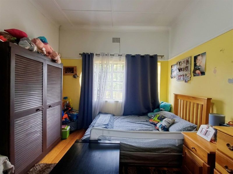 A bedroom featuring timber flooring, a window with security bars, and high ceilings, providing a functional space for rest.