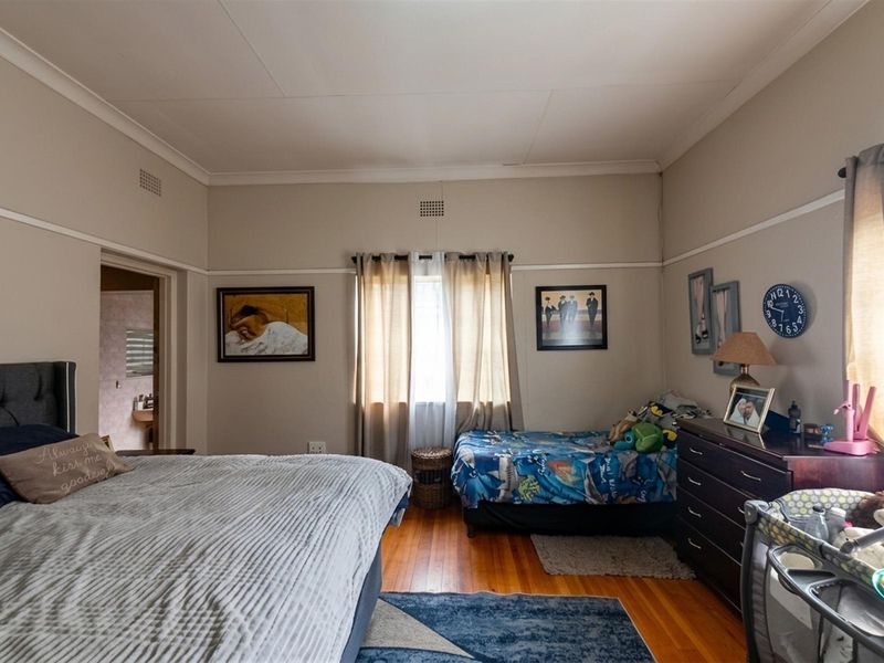 A spacious bedroom featuring original hardwood flooring, coved ceilings, and a picture rail, with an adjoining en-suite bathroom visible.