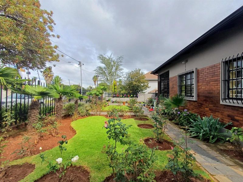 A well-maintained garden area featuring a paved walkway, established landscaping, and a brick-faced exterior wall with security bars on the windows.