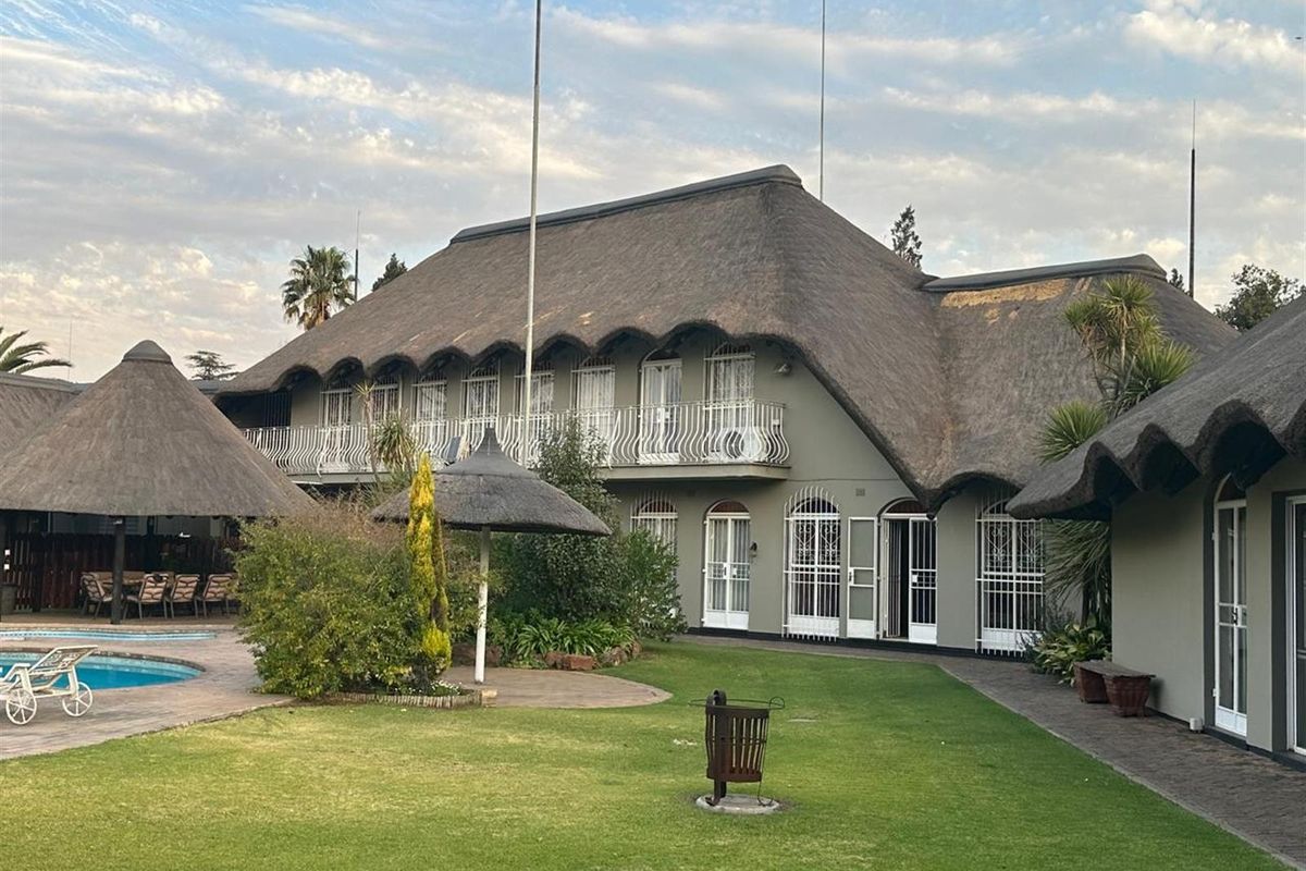 Spacious rear exterior view featuring a large thatched-roof house, a swimming pool, a manicured lawn, and a covered patio area.