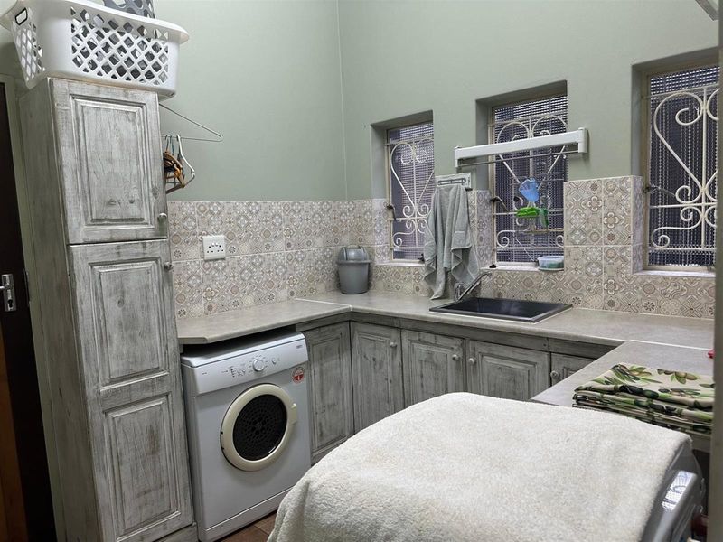 Functional laundry room featuring built-in cabinetry, a stainless steel sink, tiled backsplash, and dedicated space for laundry appliances.