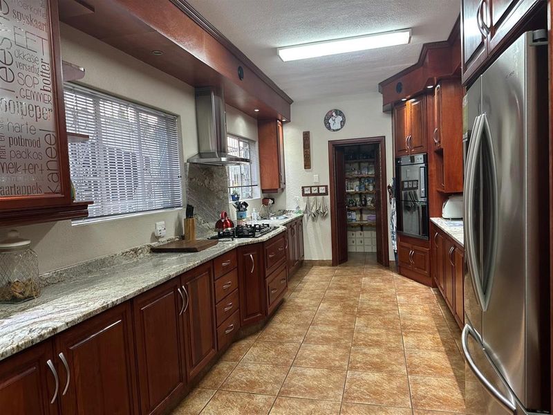 A functional kitchen featuring warm-toned wooden cabinetry, granite countertops, a gas hob with extractor, and a convenient walk-in scullery area.