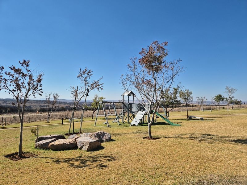 A well-maintained residential garden featuring a children's playground, manicured lawn, decorative rock features, and scenic landscape views.