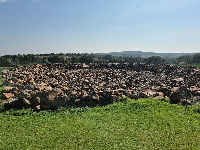 A large circular stone enclosure situated on a grassy plot, featuring perimeter fencing and expansive views of the surrounding landscape.