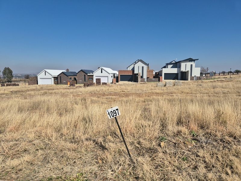 A vacant residential plot of land with a property marker, situated in a developed estate with surrounding modern homes.