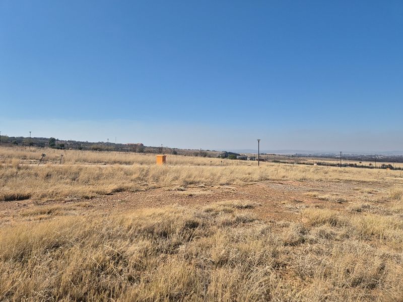 A view of a vacant residential plot featuring dry grass, street lighting, and a utility box under a clear blue sky.