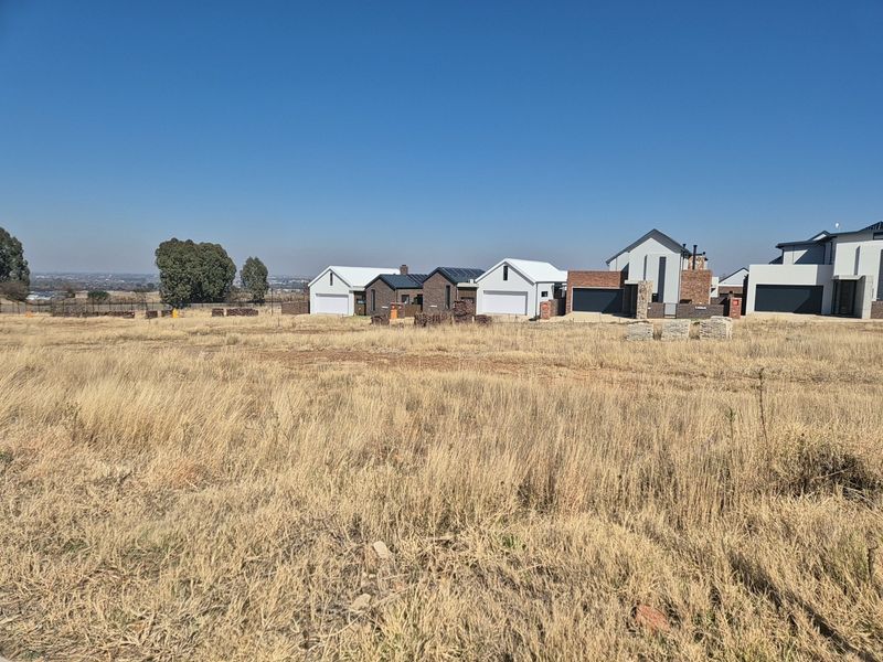 A view of a vacant residential plot with surrounding modern housing developments in the background.