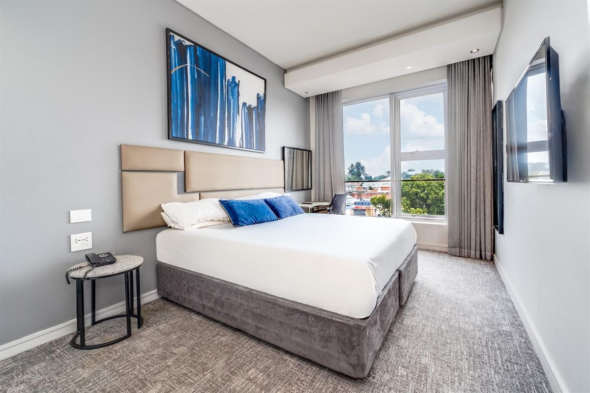 A modern, well-maintained bedroom featuring neutral carpeting, recessed ceiling lighting, and large floor-to-ceiling windows with integrated curtain tracks.