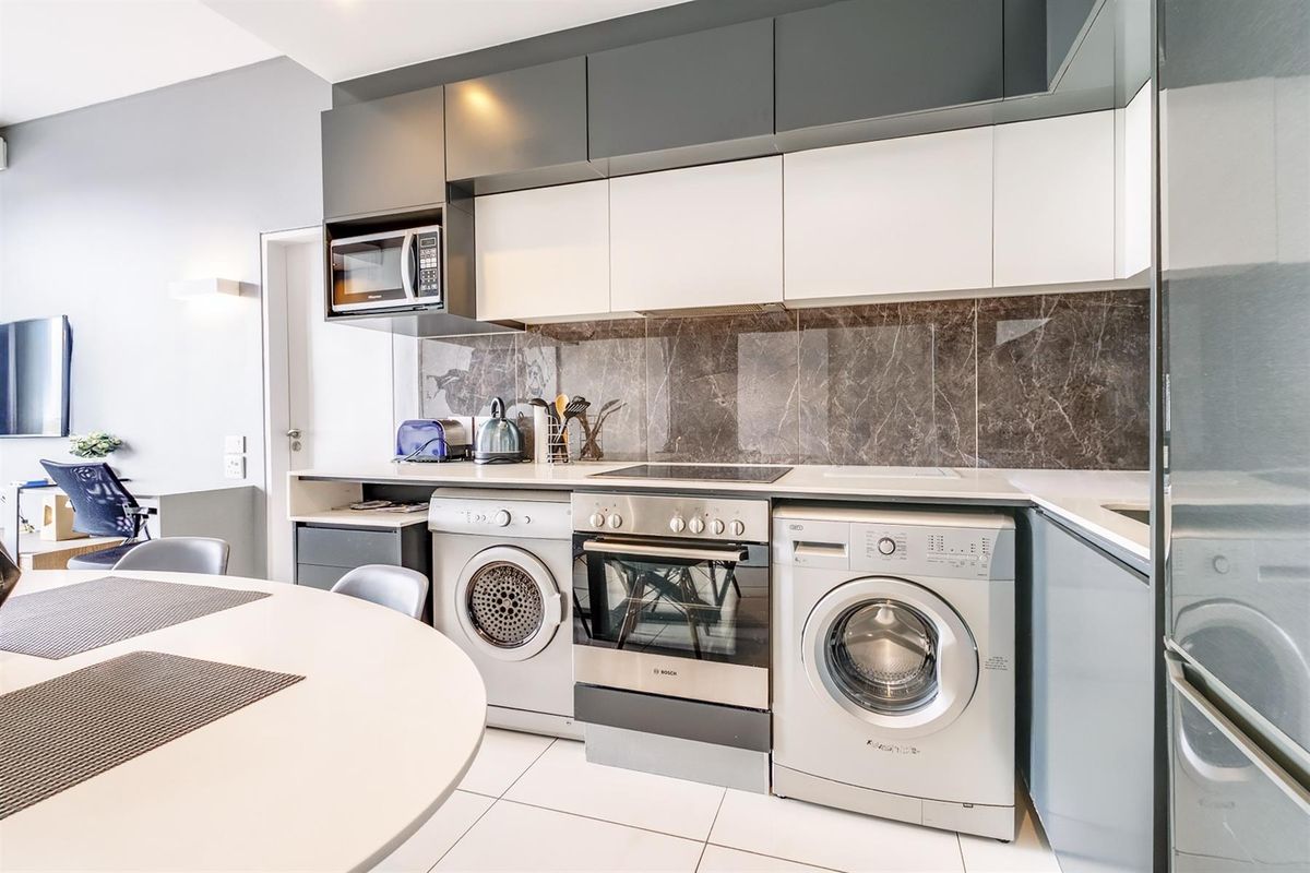 Modern kitchen featuring sleek two-tone cabinetry, stone splashback, integrated appliances, and high-quality stone countertops in an open-plan layout.