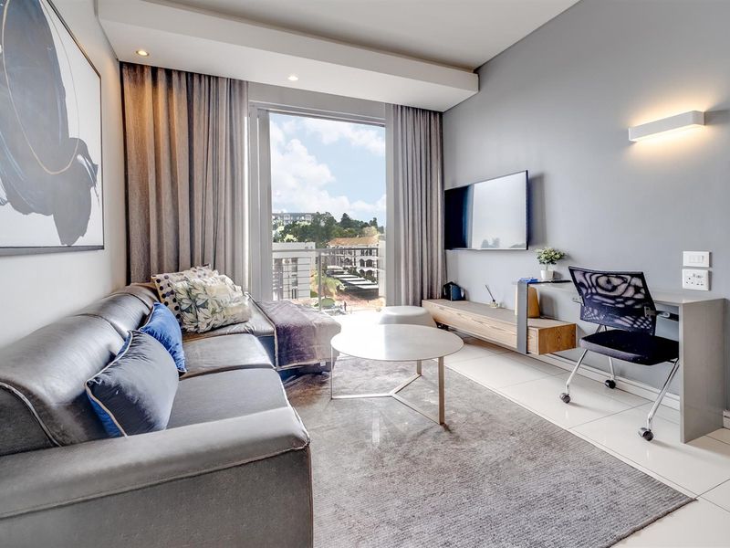 A modern living room featuring tiled floors, recessed lighting, and a built-in wall-mounted desk, with direct access to a balcony.