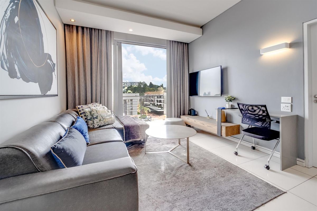 A modern living room featuring tiled floors, recessed lighting, and a built-in wall-mounted desk, with direct access to a balcony.
