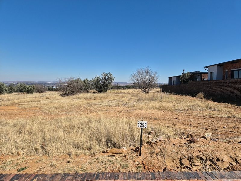 A vacant residential plot featuring dry grass, a boundary wall, and a clear view of the surrounding landscape.