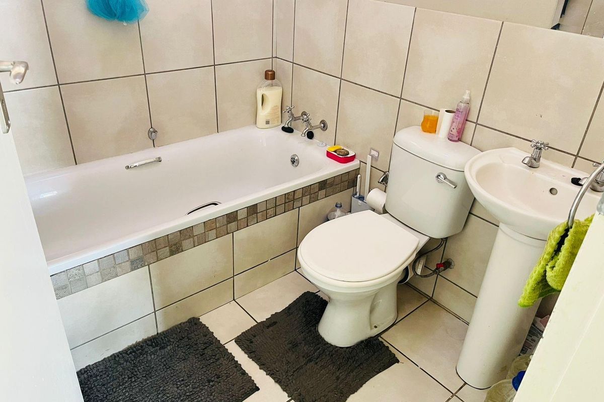 A functional bathroom featuring a standard bathtub, pedestal basin, and toilet with neutral wall and floor tiling.