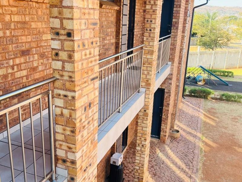 A multi-level exterior view of a face brick building featuring stainless steel balustrades, tiled balconies, and a paved ground-level walkway.