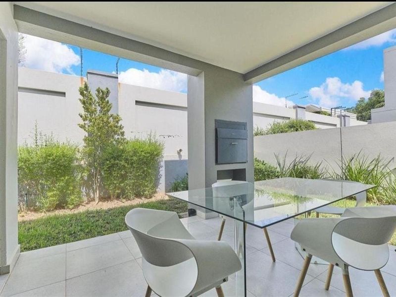 A covered patio area featuring tiled flooring and a built-in braai, overlooking a private garden space.
