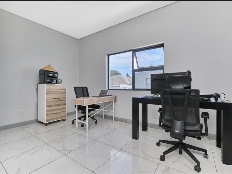 A bright home office featuring modern large-format marble-look floor tiles and a clean, neutral aesthetic with a functional window.