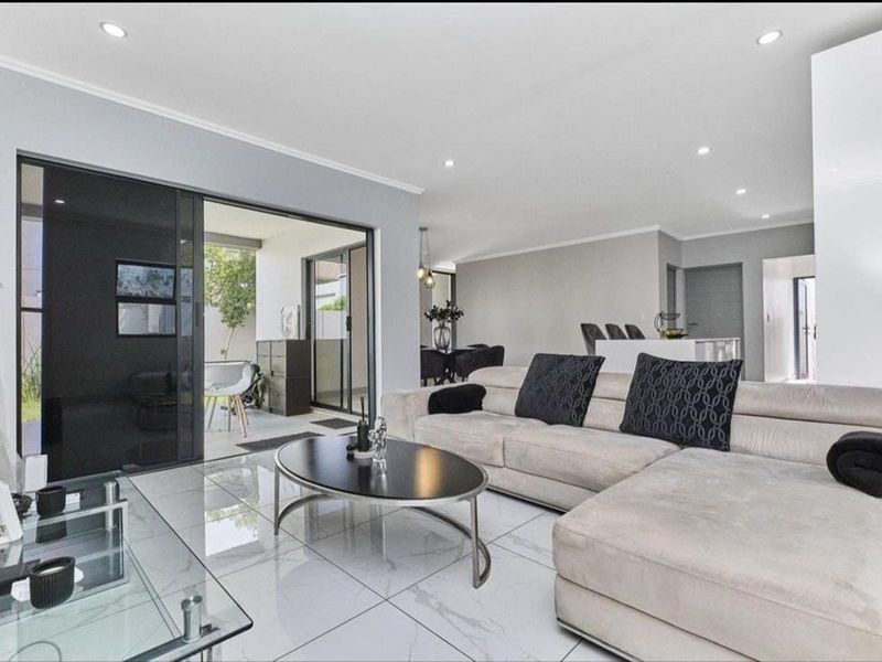 Spacious open-plan living area featuring modern porcelain floor tiles, recessed downlighting, and seamless flow to an outdoor patio through large sliding glass doors.