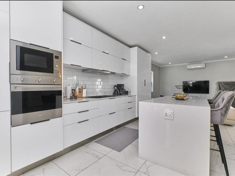 Modern open-plan kitchen featuring sleek white cabinetry, a central island, integrated appliances, subway tile backsplash, and polished porcelain flooring.