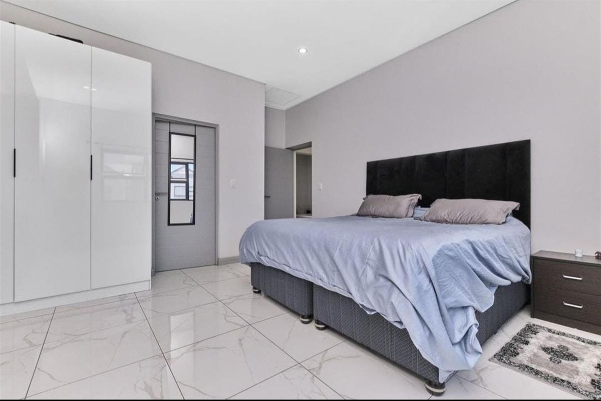 A modern bedroom featuring large-format marble-look floor tiles, built-in white cabinetry, and neutral wall finishes.