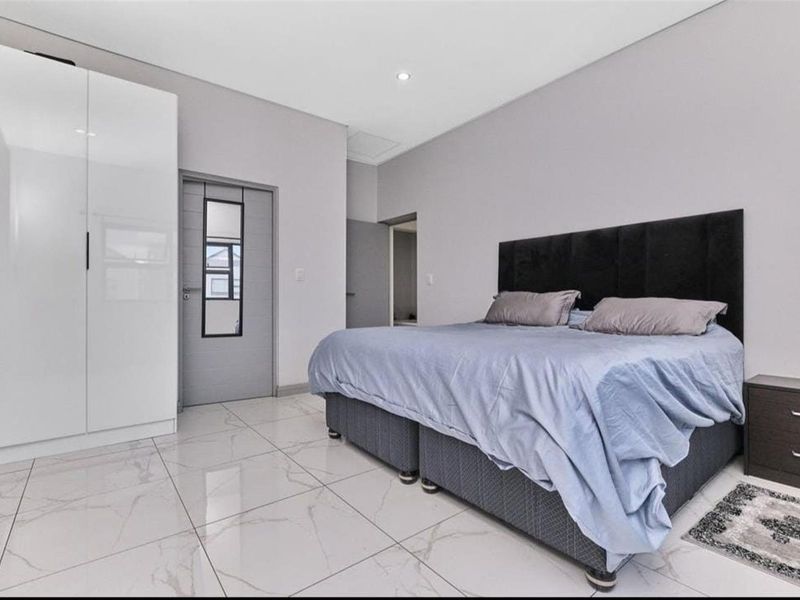 A modern bedroom featuring large-format marble-look floor tiles, built-in white cabinetry, and neutral wall finishes.