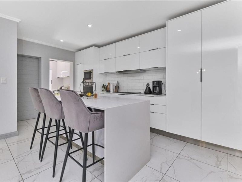 Modern kitchen featuring sleek white cabinetry, a central island with breakfast bar seating, stone countertops, and high-quality porcelain floor tiles.