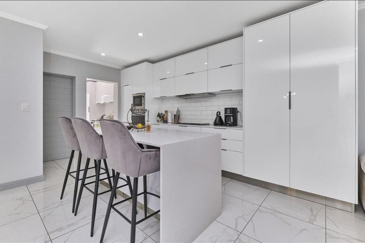 Modern kitchen featuring sleek white cabinetry, a central island with breakfast bar seating, stone countertops, and high-quality porcelain floor tiles.
