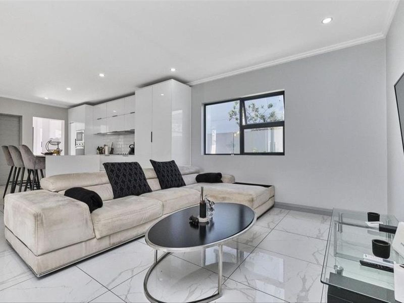 Modern open-plan living area featuring sleek white cabinetry, marble-look tiled flooring, and recessed lighting, seamlessly connecting the kitchen and lounge space.