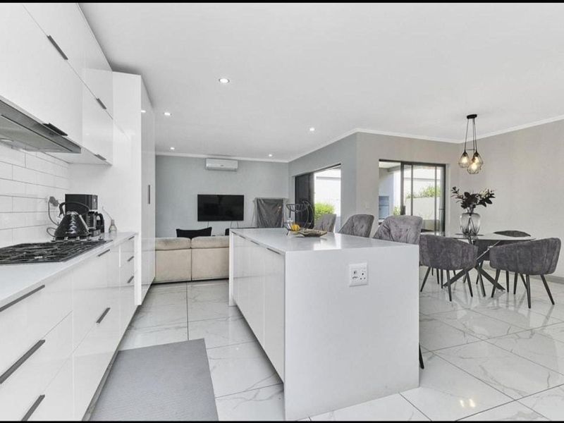 Modern open-plan living area featuring a sleek kitchen with island, high-gloss cabinetry, gas cooktop, and seamless flow to the outdoor patio through sliding doors.