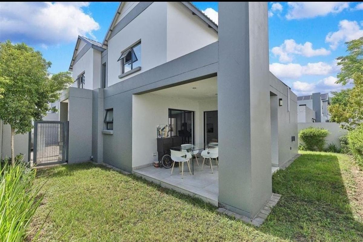 Rear view of the townhouse featuring a covered patio with tiled flooring, sliding glass doors, and a private garden area.
