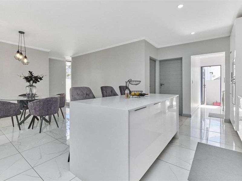 Modern open-plan kitchen and dining area featuring a central island, high-gloss cabinetry, and sleek porcelain floor tiles throughout.