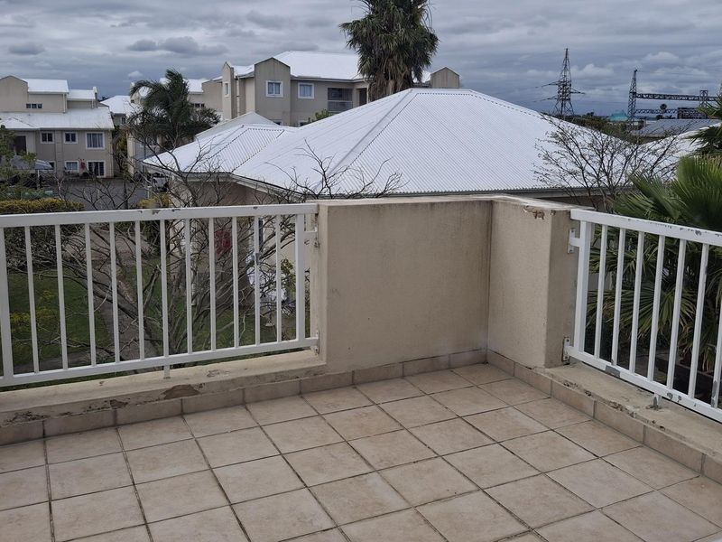 An open-air balcony featuring tiled flooring and a metal balustrade, offering views of the surrounding townhouse complex.