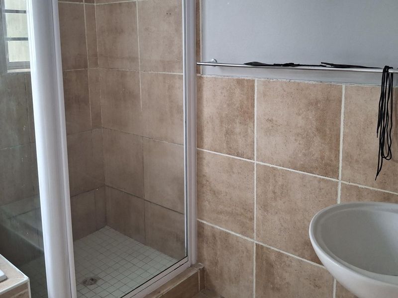A functional bathroom featuring a shower enclosure, bathtub, and pedestal basin with neutral wall tiling.