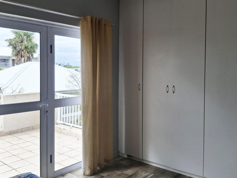 A bright bedroom featuring built-in cupboards, laminate flooring, and a glass door providing direct access to an outdoor balcony area.