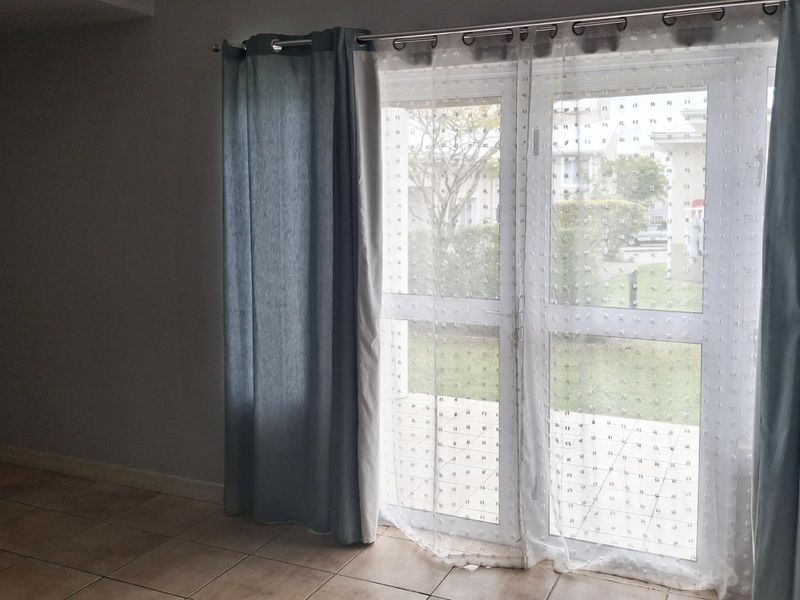An empty living room area featuring tiled flooring and a double glass door providing access to the exterior.