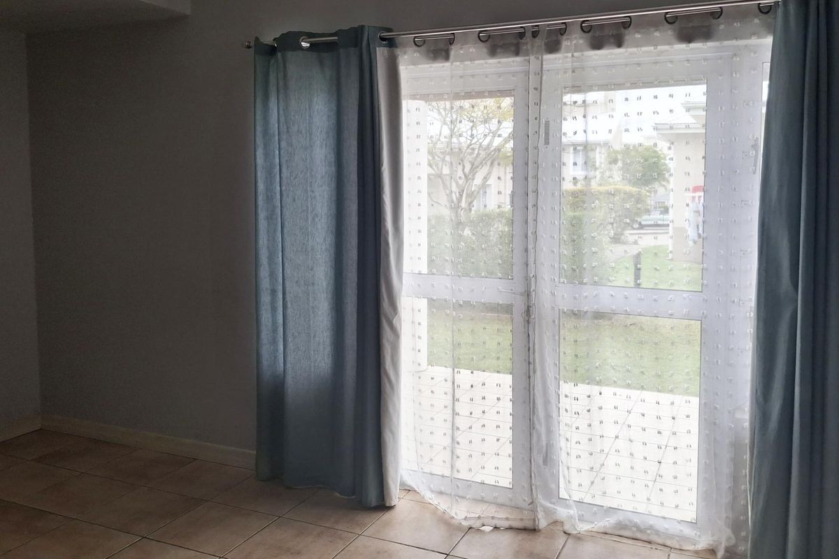 An empty living room area featuring tiled flooring and a double glass door providing access to the exterior.