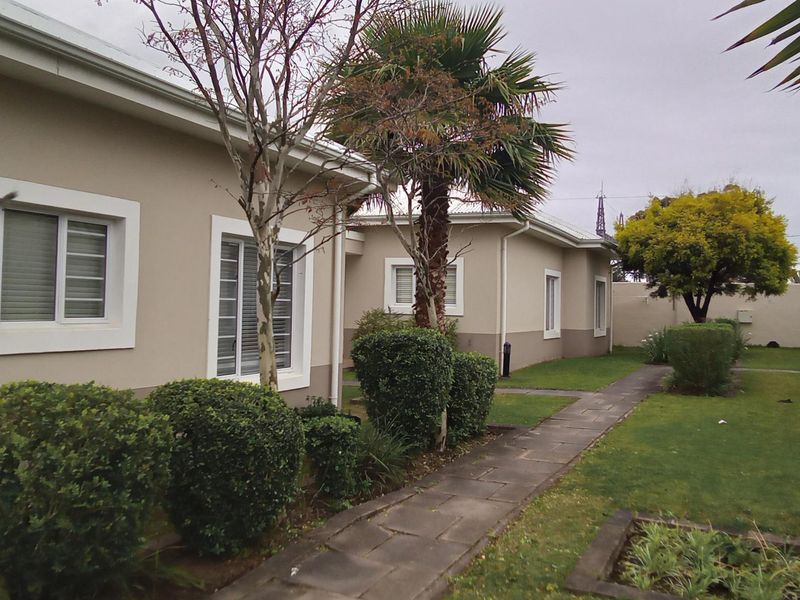 A view of the rear exterior of the townhouse, featuring a paved walkway, well-maintained garden, and windows with security bars.