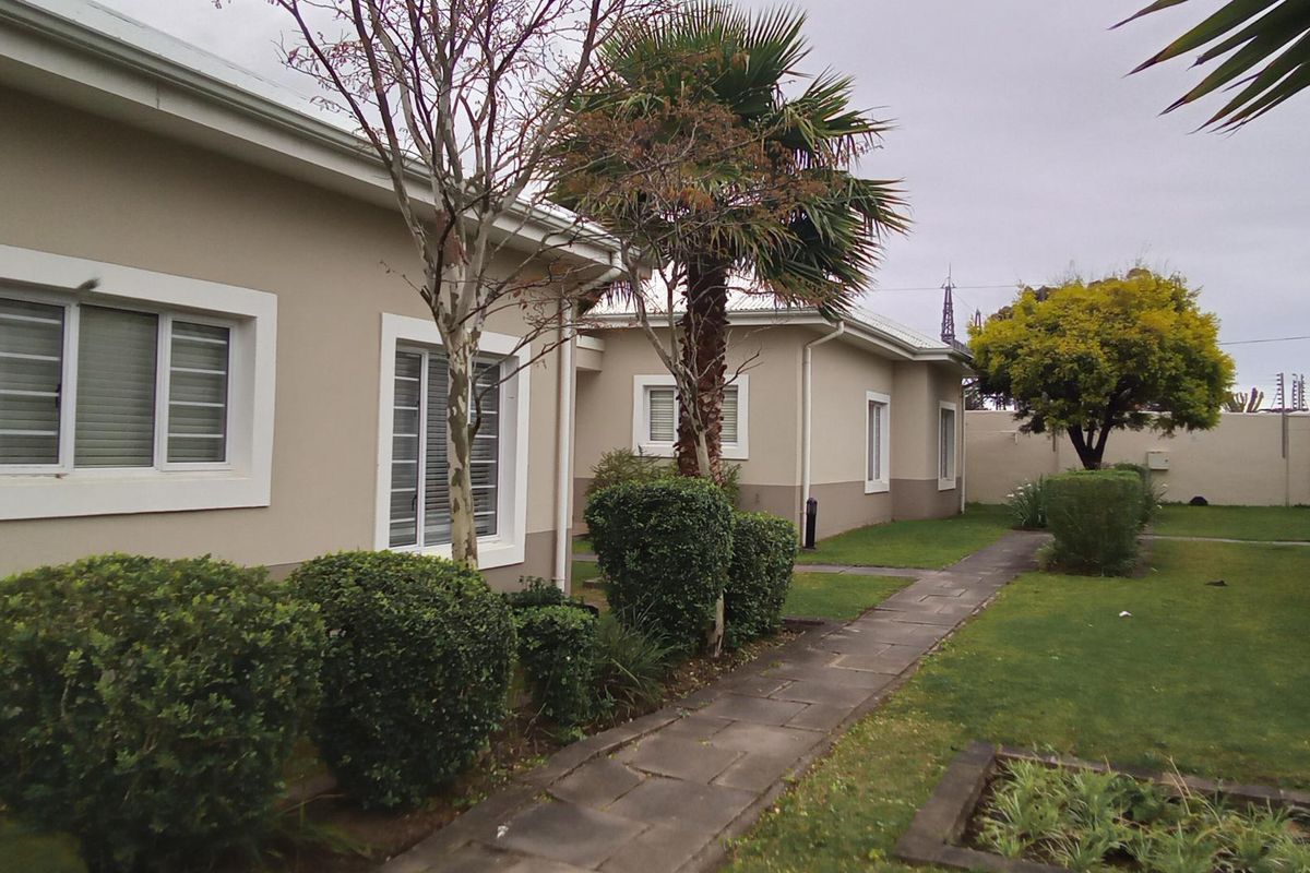 A view of the rear exterior of the townhouse, featuring a paved walkway, well-maintained garden, and windows with security bars.