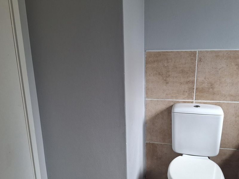 A functional bathroom featuring a standard toilet and tiled wall surround with a bathtub.