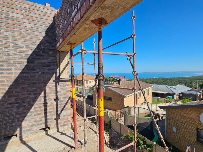 An exterior view of a property under construction, featuring exposed brickwork, scaffolding, and support props with a coastal view in the background.