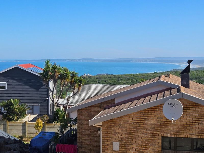 Elevated coastal view overlooking the ocean and surrounding residential neighborhood, featuring brick and timber-clad exterior structures.