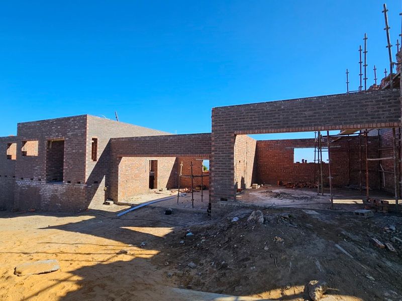 A view of a residential property currently under construction, featuring exposed brick walls and scaffolding on a cleared building site.