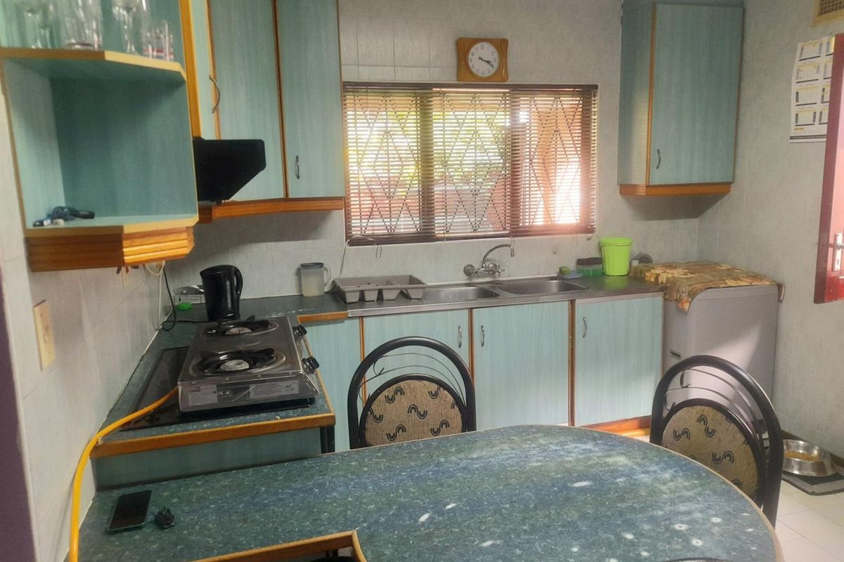 A dated kitchen featuring laminate countertops, built-in cabinetry, a double sink, and a window with blinds.