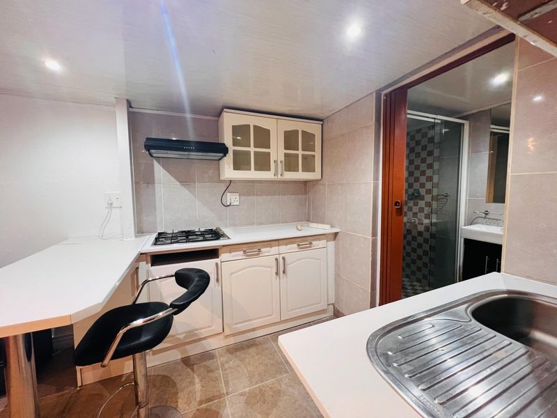 Compact kitchen featuring built-in cabinetry, gas hob, extractor fan, and stainless steel sink, with adjacent bathroom access.