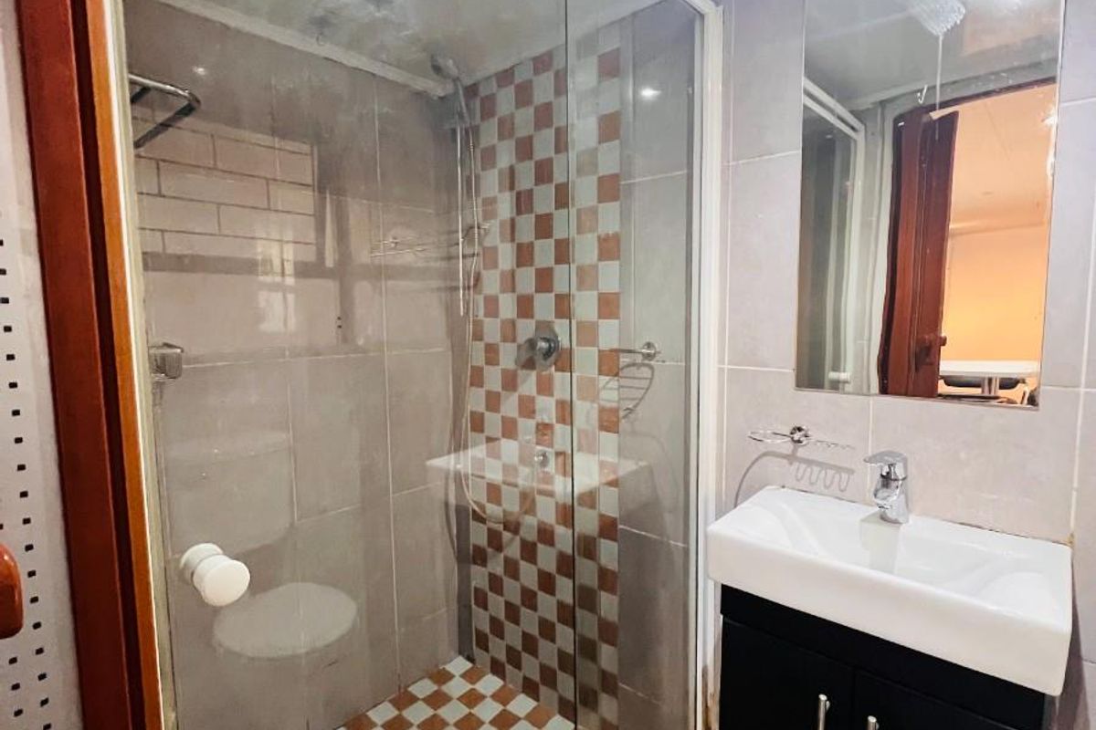 Compact bathroom featuring a glass-enclosed shower, modern wall-mounted vanity with basin, and tiled finishes throughout.