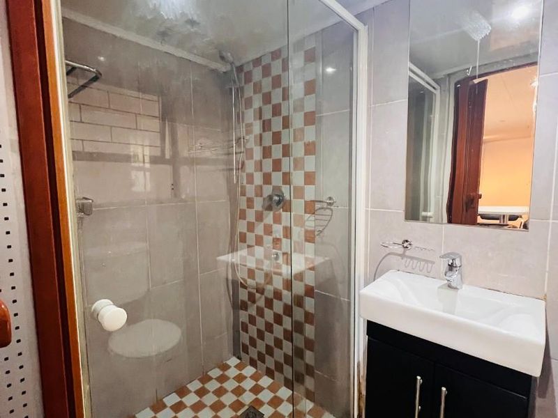 Compact bathroom featuring a glass-enclosed shower, modern wall-mounted vanity with basin, and tiled finishes throughout.