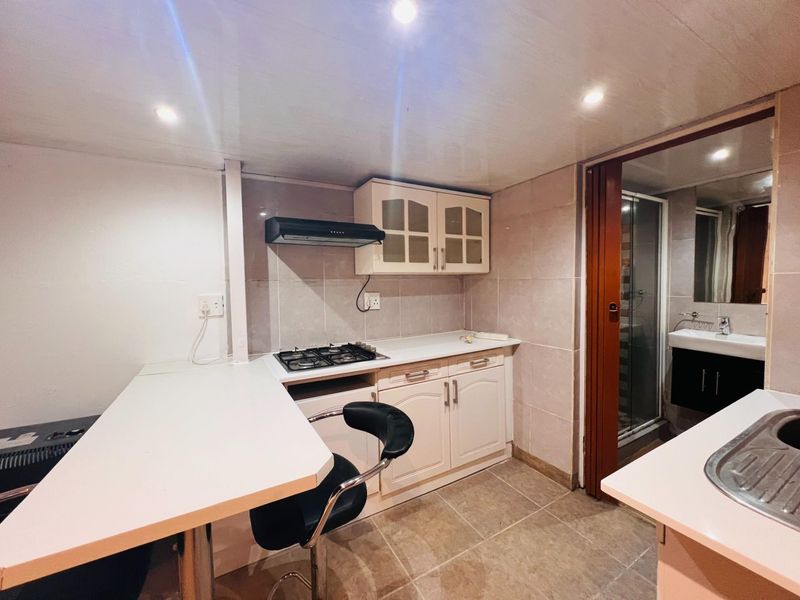 Compact kitchen featuring built-in cabinetry, gas hob, extractor fan, and tiled finishes, with an adjacent bathroom area visible through the doorway.